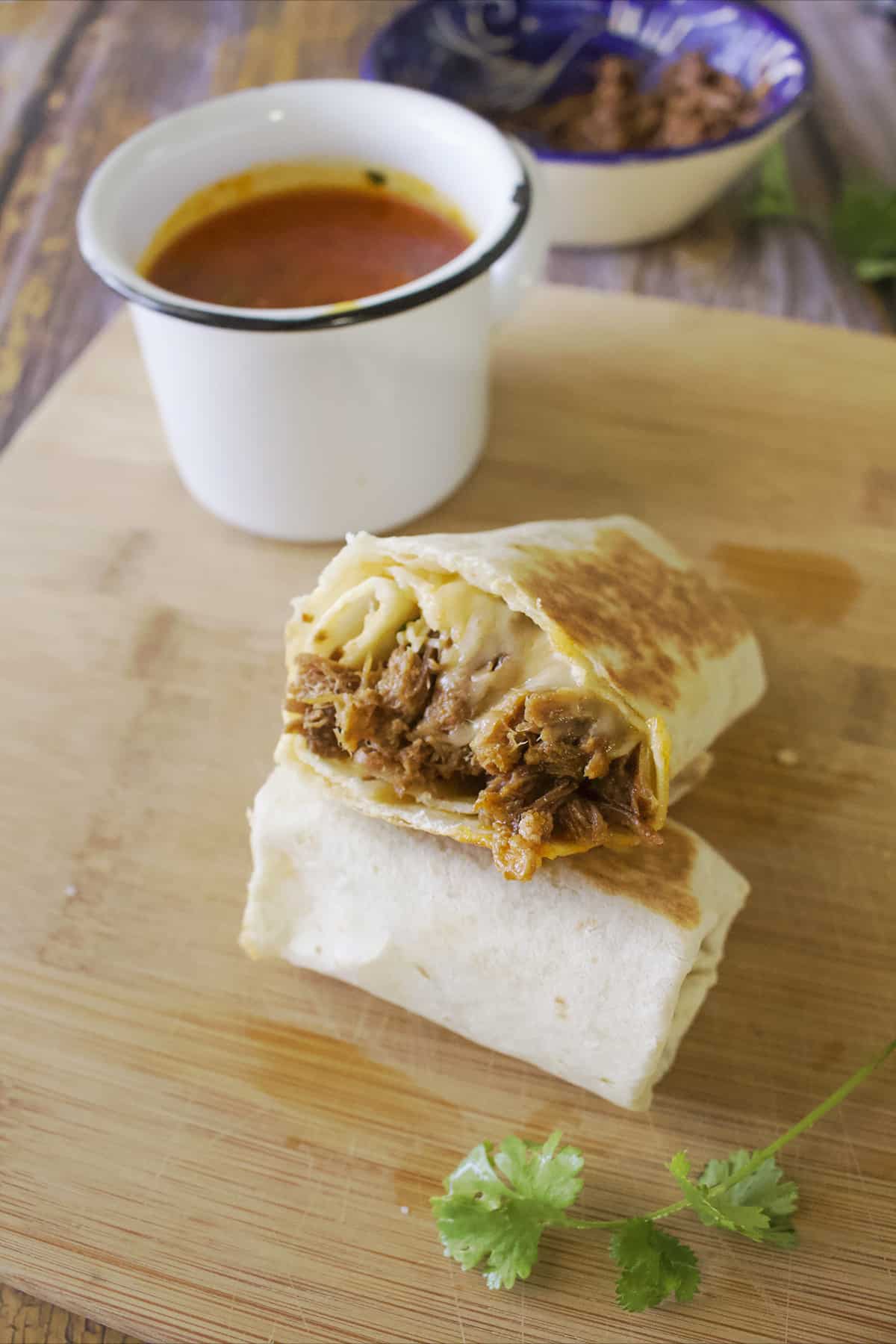 A birria burrito cut in half next to consomme.