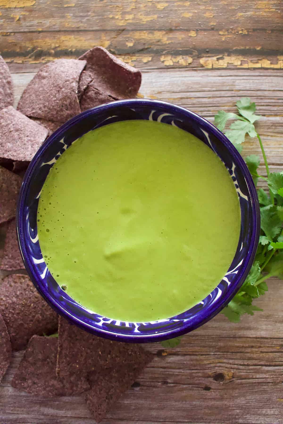 A bowl of jalapeno salsa next to chips and cilantro.