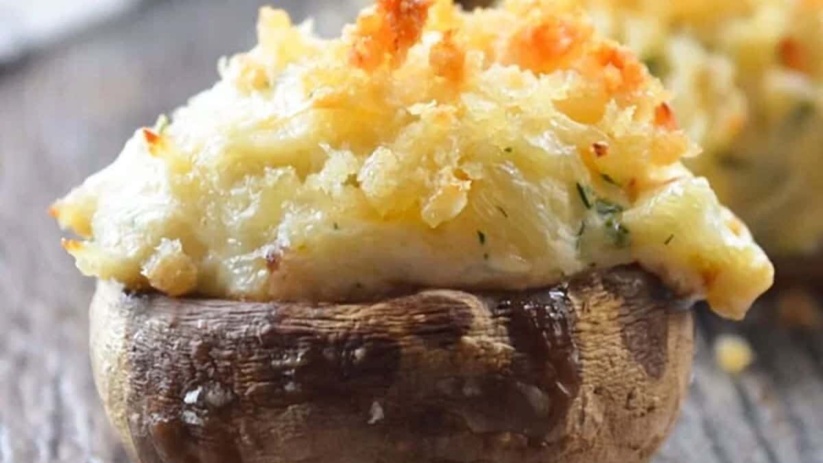 Stuffed mushroom with a golden, crispy cheese and herb topping sitting on a rustic wooden surface.