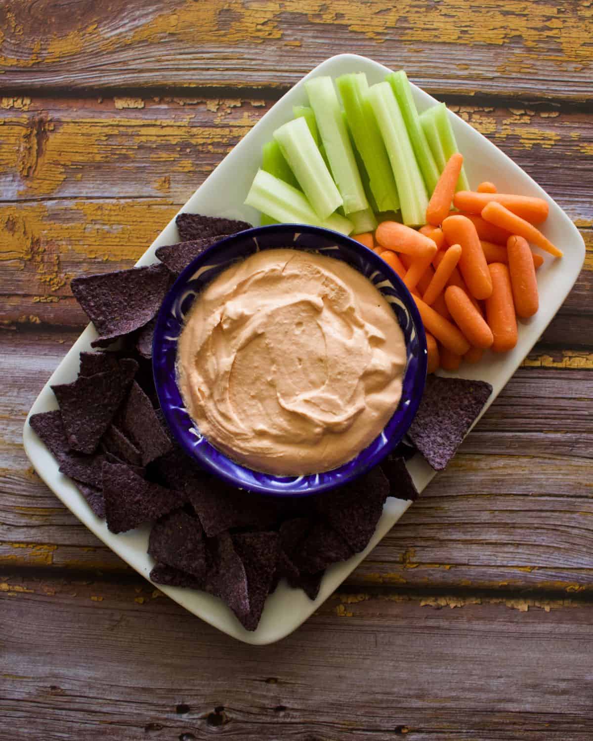 Cream cheese and salsa dip served in a blue bowl surrounded by veggie dippers and chips.