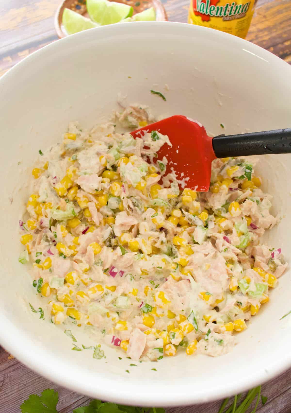 Mixing the ingredients with a red rubber spatula in a large white bowl.