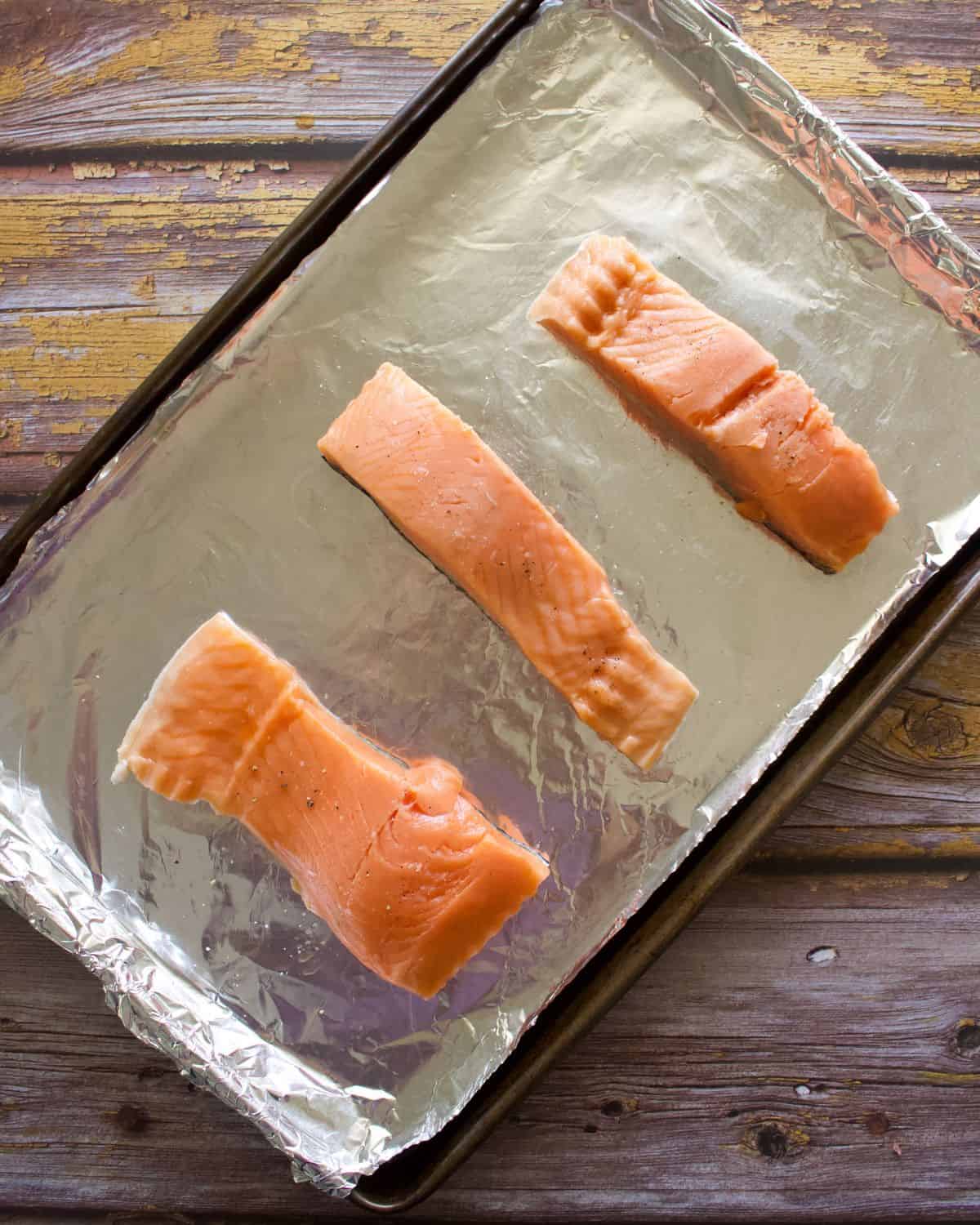 A sheet pan with raw salmon filets.
