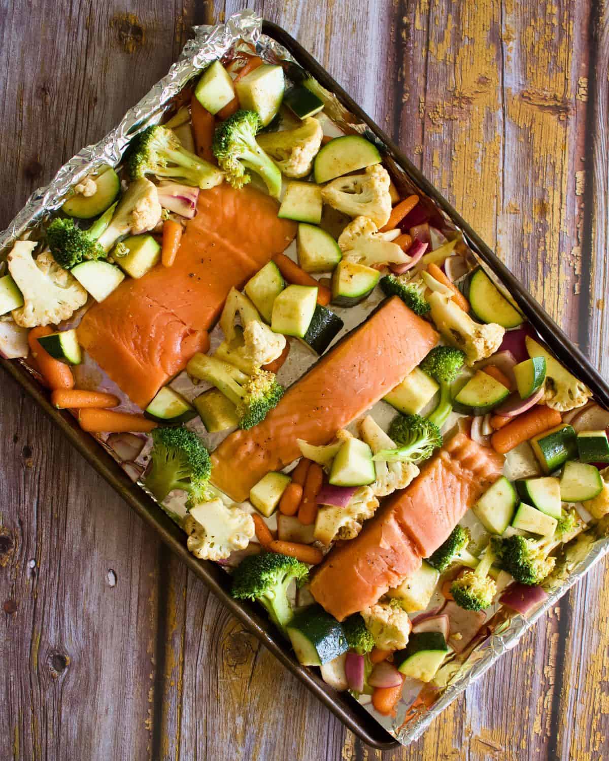 A sheet pan with salmon and vegetables ready for the oven.