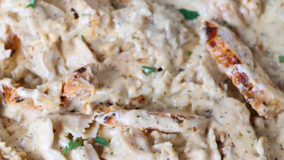 Close-up of creamy chicken pasta featuring grilled chicken strips and pasta coated in a rich, creamy sauce. Garnished with fresh herbs.