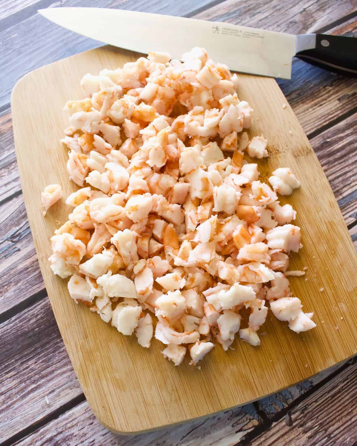 Cooked shrimp chopped into small pieces on a wooden cutting board.