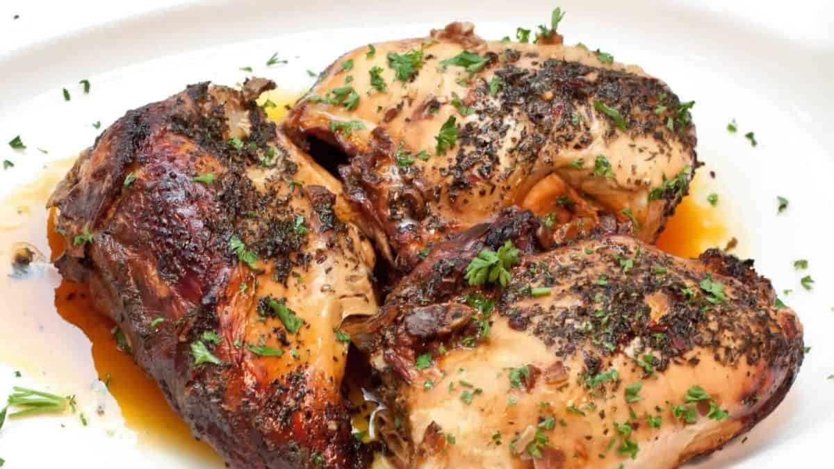 Three pieces of roasted chicken seasoned with herbs are placed on a white plate. The chicken is garnished with chopped parsley, and the dish appears juicy and tender.