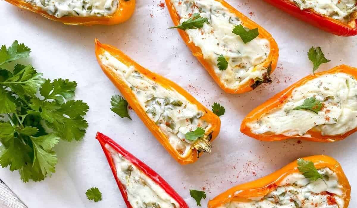 Colorful bell pepper halves filled with a creamy mixture, garnished with cilantro and a sprinkle of paprika, on a white surface with a bunch of cilantro on the side.