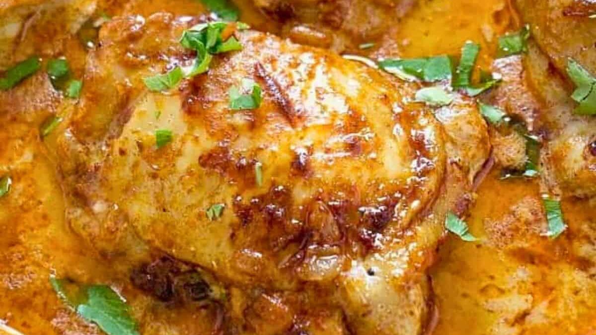 Cooked chicken thighs in a rich, golden curry sauce, garnished with freshly chopped cilantro. The sauce is thick and creamy, coating the browned chicken with a glossy finish.