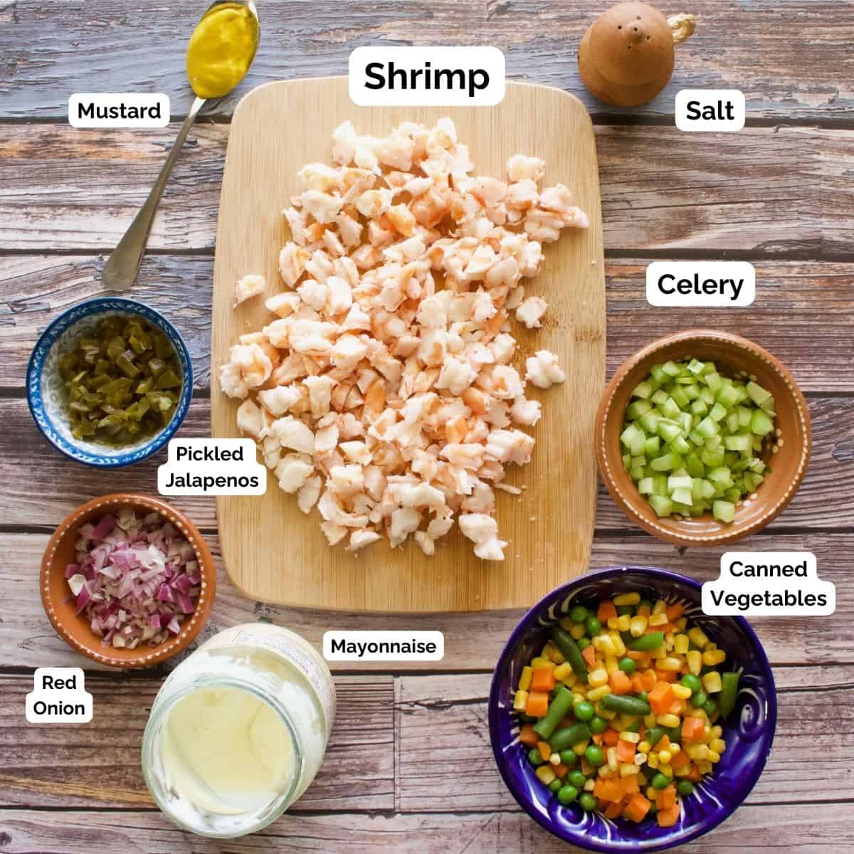 The ingredients needed to make the shrimp salad labeled and sitting on a wooden table.
