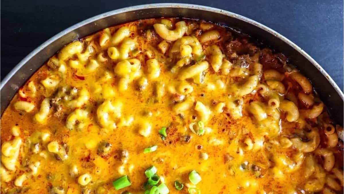 A close-up of a skillet filled with baked macaroni and cheese topped with melted cheddar and ground beef, garnished with chopped green onions.