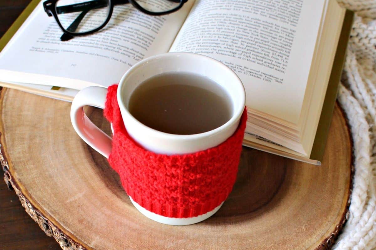 A cup of oregano tea on a wooden surface next to a book and glasses.