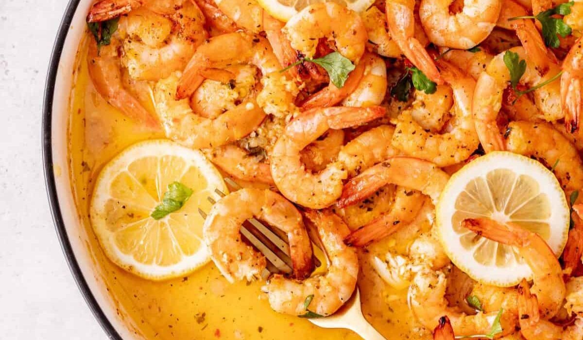 Cooked shrimp in a creamy garlic butter sauce, garnished with fresh parsley and lemon slices, served in a skillet with a white spoon.
