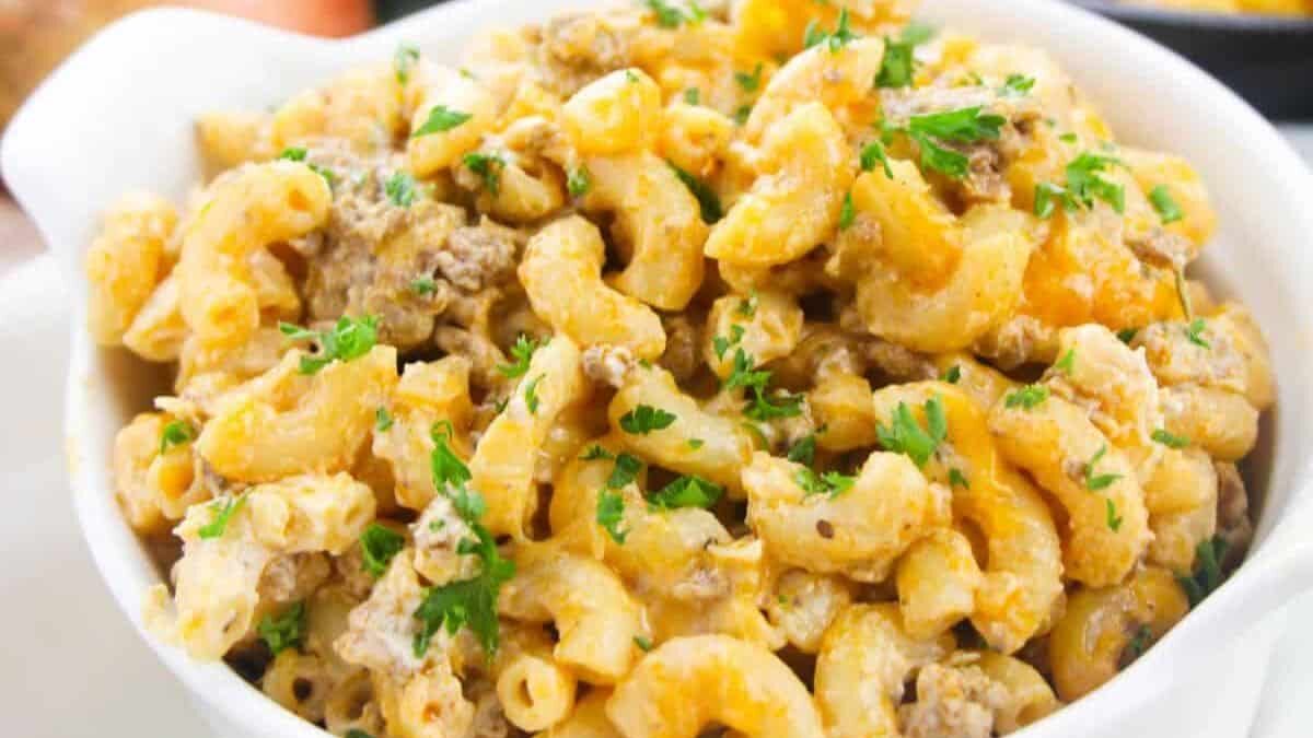 A close-up of a bowl filled with creamy macaroni and cheese, topped with ground beef and garnished with fresh parsley. The dish is served in a white bowl, highlighting its golden and textured appearance.