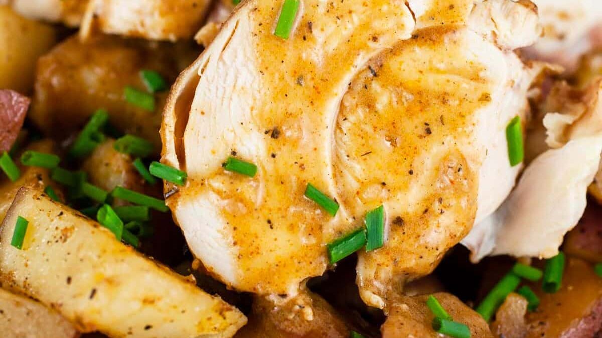 Close-up view of sliced roasted chicken with a seasoned brown sauce. The chicken is garnished with chopped chives and served over roasted potato wedges, creating a savory and appetizing dish.