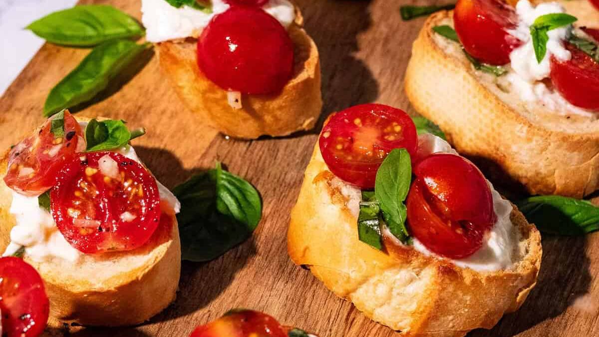 Close-up of bruschetta topped with sliced cherry tomatoes, fresh basil leaves, and creamy mozzarella cheese on toasted baguette slices, all arranged on a wooden board.