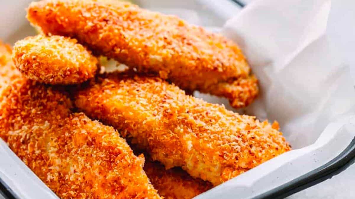 A tray of crispy, golden-brown breaded chicken tenders, placed on a paper liner. The tenders are neatly arranged and appear freshly cooked, with a crunchy texture visible.