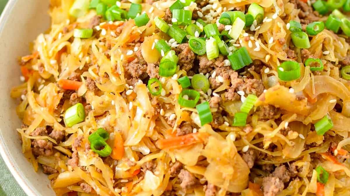 A close-up of a dish featuring stir-fried cabbage, ground meat, and sliced green onions. The dish is garnished with sesame seeds and finely chopped scallions. The vibrant mix of ingredients creates a colorful and appetizing meal.
