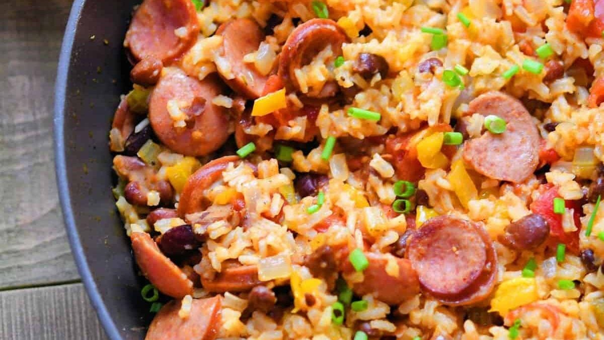 A skillet filled with Rice and sausage jambalaya, featuring sliced sausages, kidney beans, chopped peppers, and garnished with green onions. The dish is colorful and appears flavorful and hearty.
