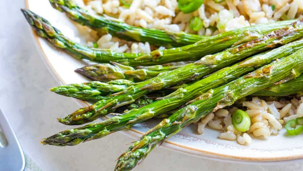 A plate of grilled asparagus spears served over a bed of rice mixed with green peas. The asparagus is lightly charred, giving it a fresh and appetizing appearance.