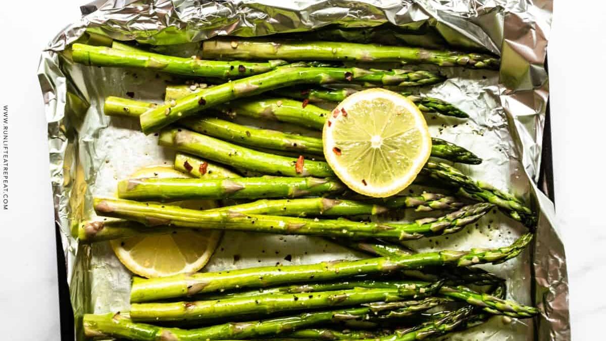 Fresh asparagus spears seasoned with pepper and topped with lemon slices are arranged on a foil-lined baking sheet.