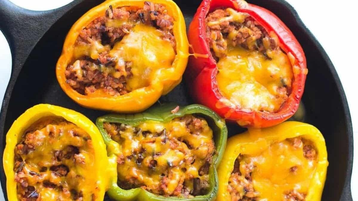 A cast iron skillet filled with red, yellow, and green bell peppers stuffed with a savory meat and rice mixture, topped with melted cheese.