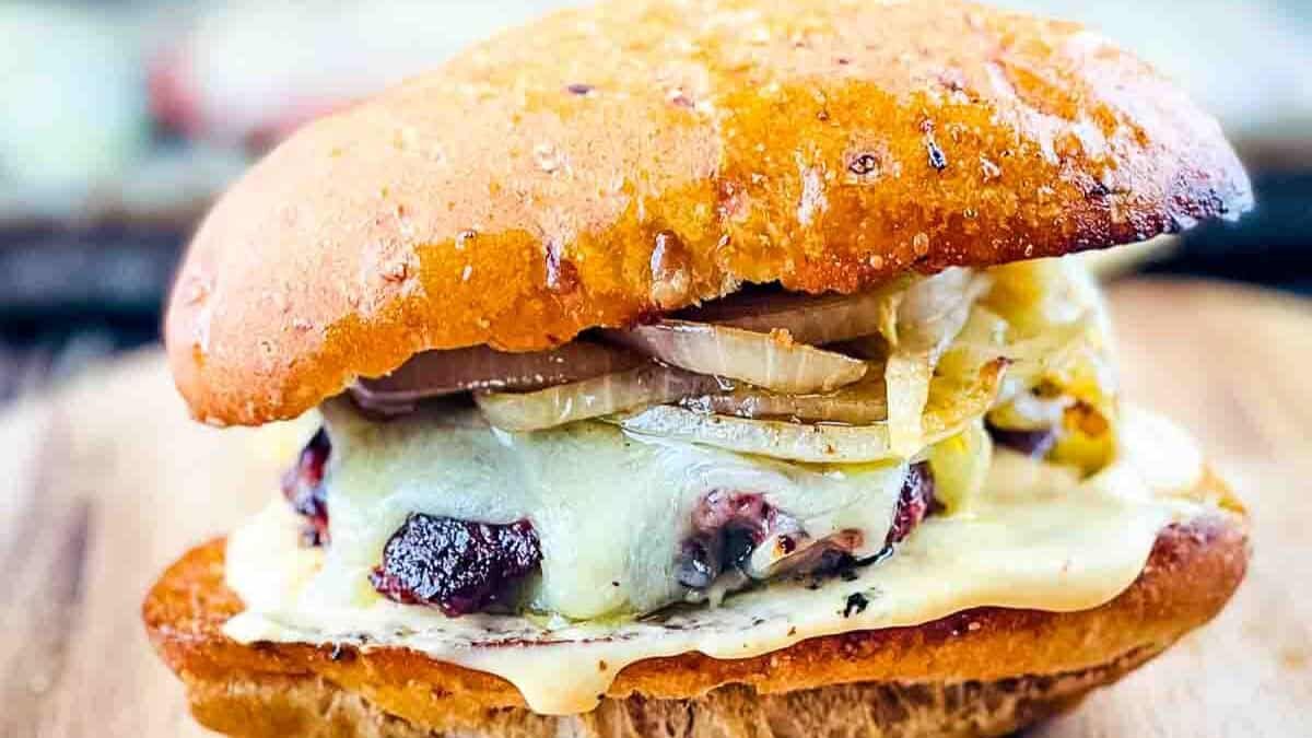 A close-up of a gourmet burger with melted cheese and caramelized onions, sandwiched between a glossy toasted bun. The burger sits on a wooden surface, highlighting its juicy and enticing appearance.