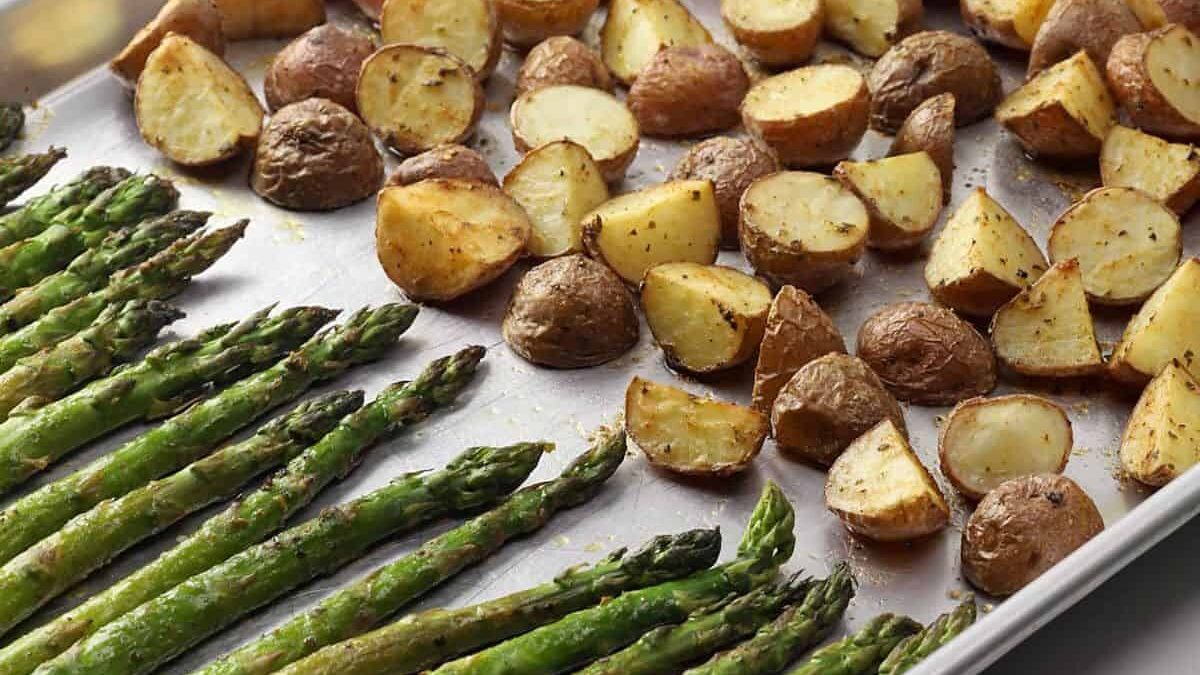 A baking tray with roasted asparagus spears and halved roasted potatoes. The vegetables are evenly spread, showing a golden-brown texture on the potatoes and vibrant green asparagus.