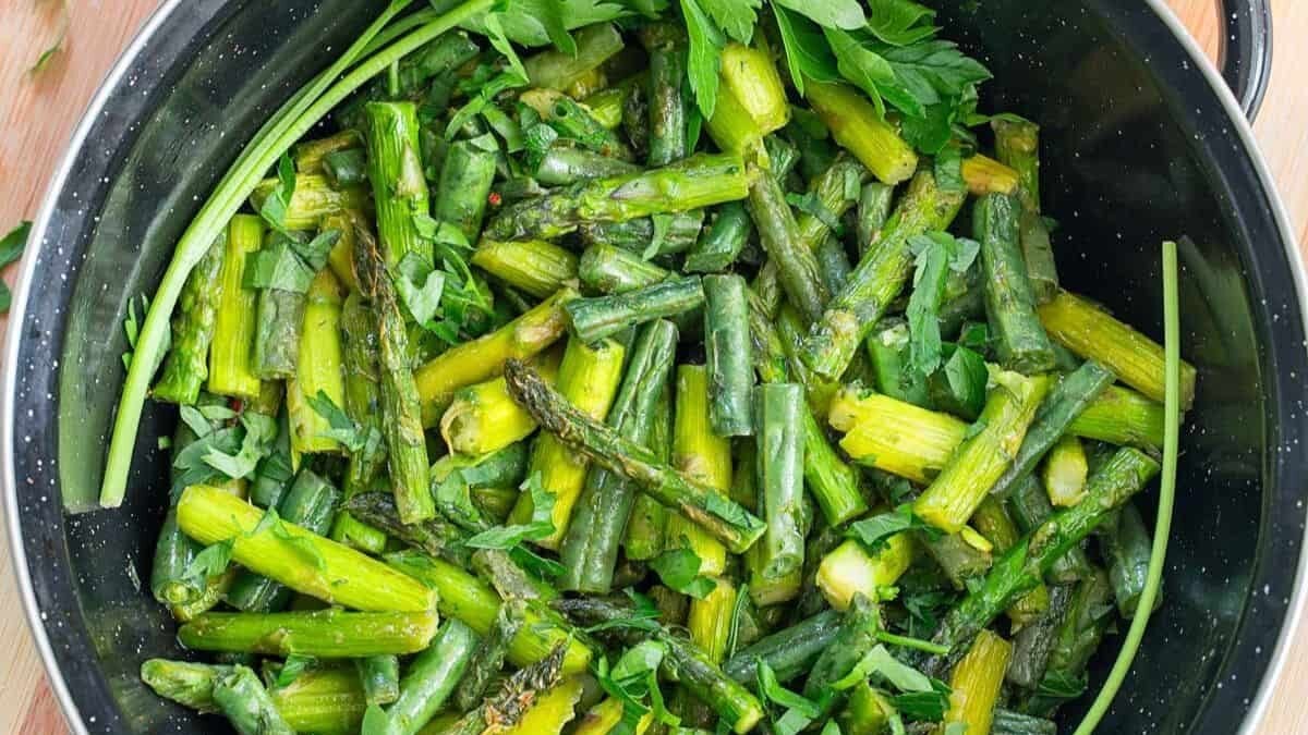 A pot filled with sautéed asparagus pieces, garnished with fresh parsley leaves. The asparagus stalks appear cooked and are mixed with vibrant green parsley, providing a fresh and healthy dish.