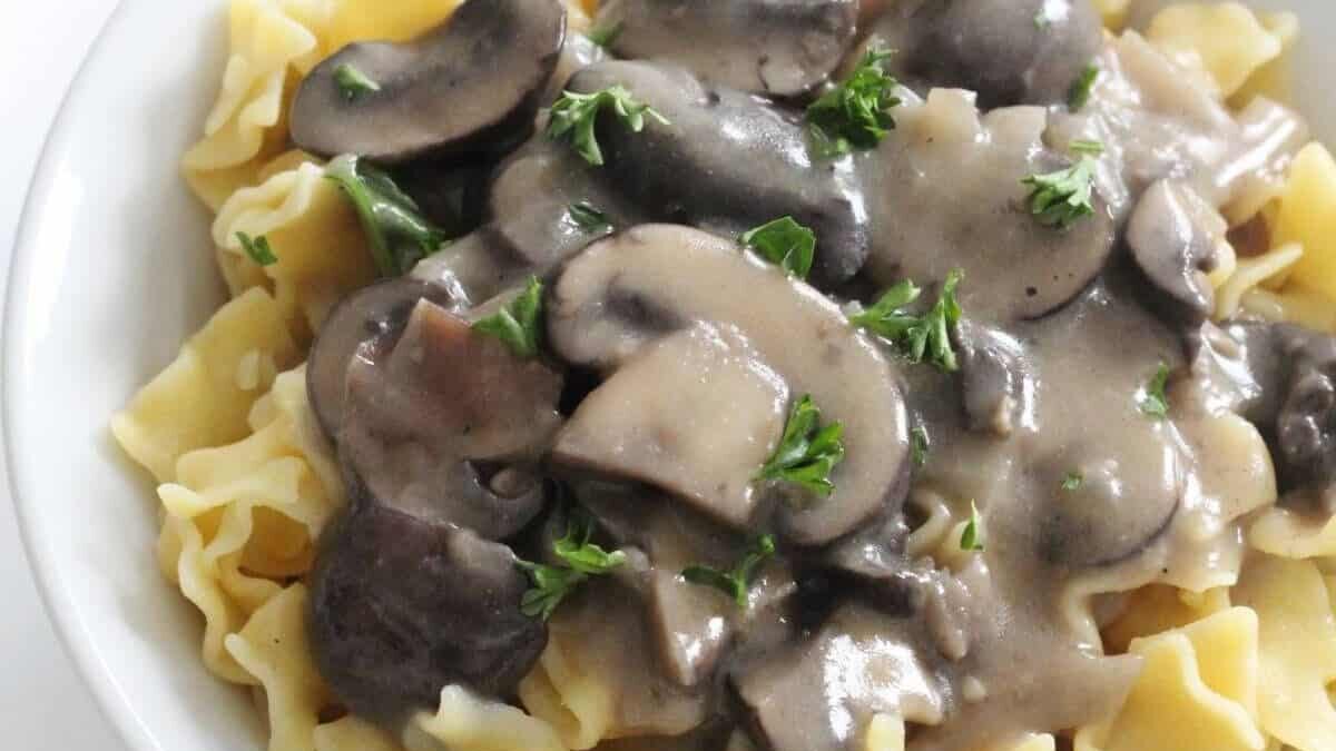 A bowl of pasta topped with creamy mushroom sauce and garnished with fresh parsley. The pasta is ribbon-shaped, and the mushrooms are sliced. The dish has a rich, savory appearance.