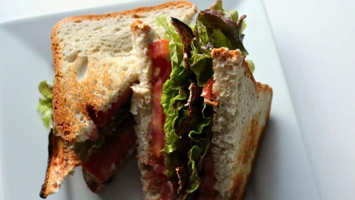 A sandwich cut in half, placed on a white plate. It has toasted bread, green lettuce, and slices of tomato visible between the bread slices.