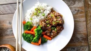 Asian Beef Stew served on a plate next to rice and veggies.