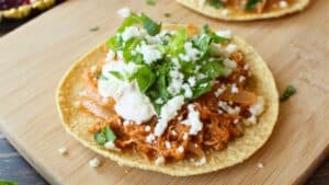 A chicken tinga tostada topped with green lettuce and sitting on a cutting board.