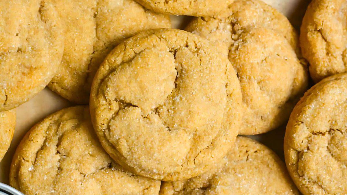 A close-up of freshly baked peanut butter cookies arranged in a pile. The cookies have a golden-brown color with a slightly cracked surface, showing a soft and chewy texture.