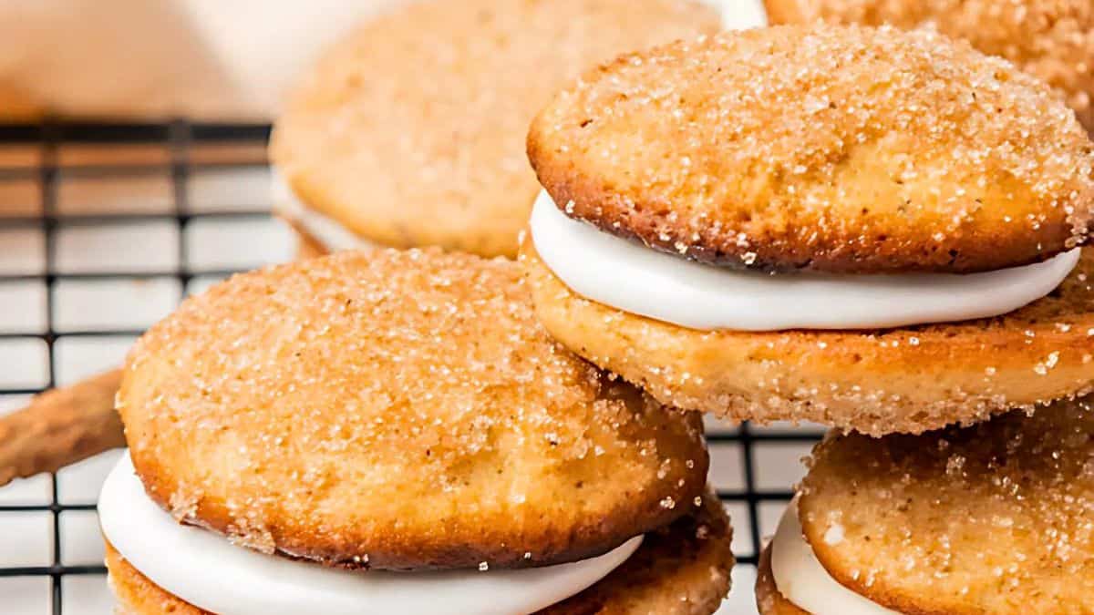 Close-up of cinnamon sugar sandwich cookies filled with cream, stacked on a cooling rack. The cookies are golden brown, dusted with sugar and cinnamon, with visible creamy white filling.