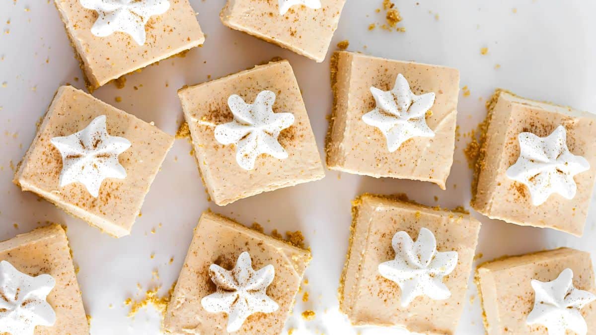 Overhead view of pumpkin pie bars topped with dollops of whipped cream and sprinkled with cinnamon on a white surface.
