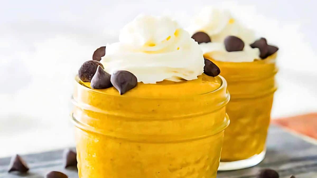 Two small glass jars filled with creamy pumpkin mousse are topped with whipped cream and chocolate chips. They are set against a light background, emphasizing the dessert's texture and inviting presentation.