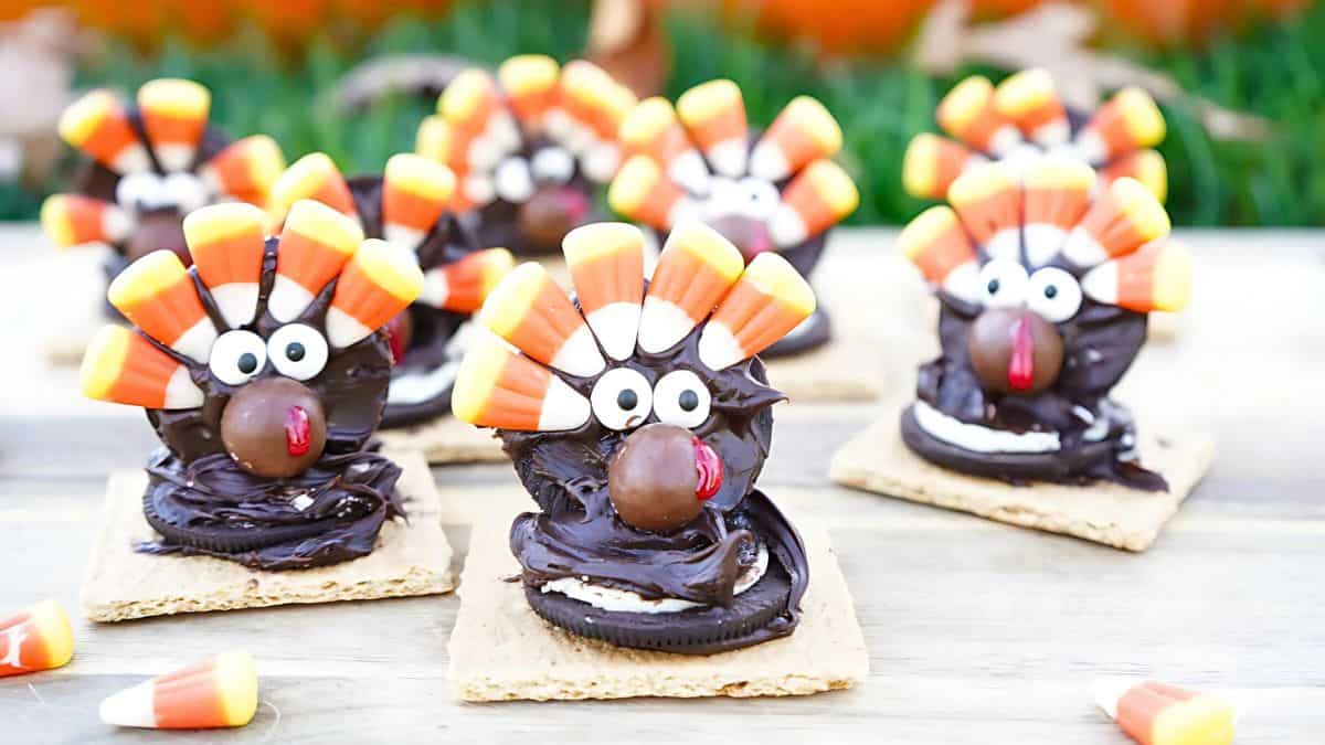 Festive turkey-themed treats made with graham crackers, Oreos, candy corn, chocolate frosting, and candy eyes, arranged on a wooden surface.