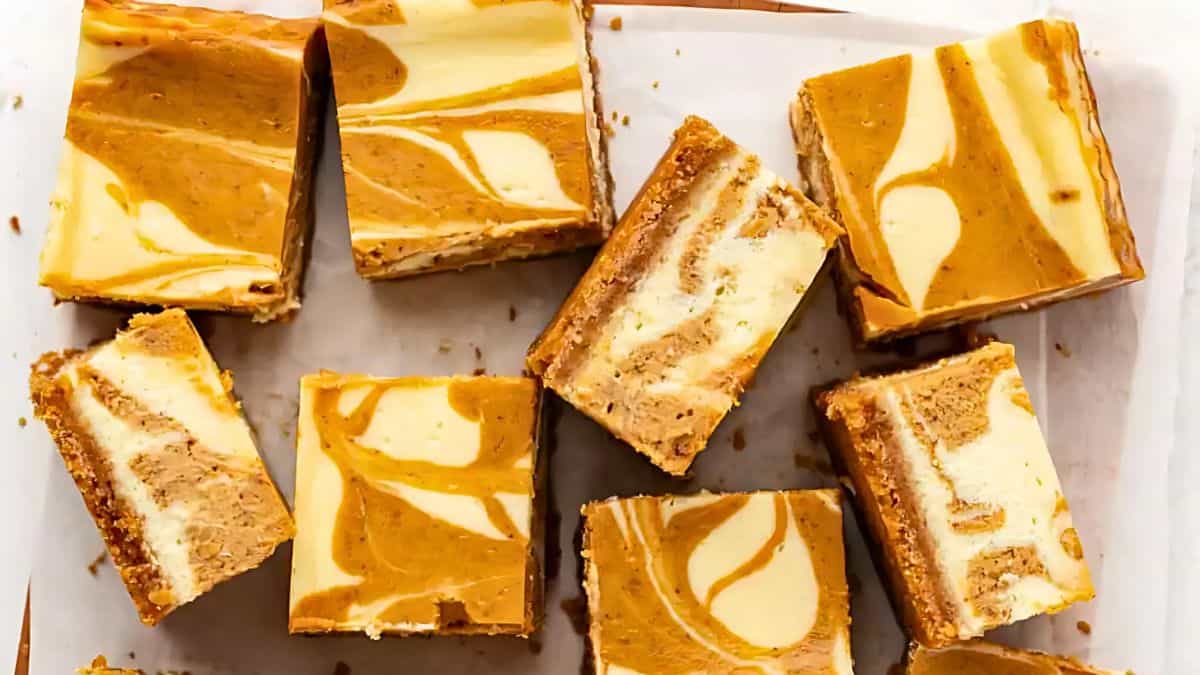 Slices of marble cheesecake bars with a swirl of caramel and cream cheese on a parchment-lined surface. The bars have a layered texture with a creamy, marbled appearance.