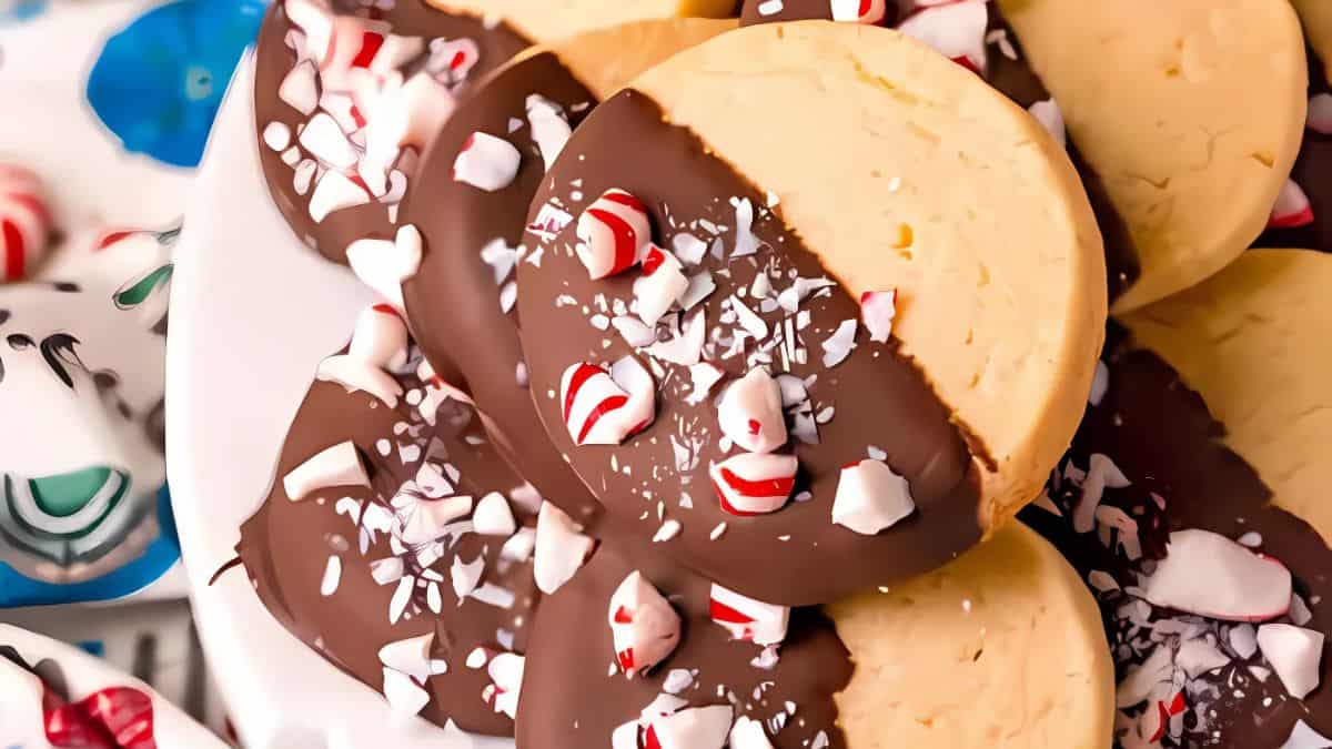 A close-up of chocolate-dipped cookies on a plate. The cookies are partially coated with dark chocolate and sprinkled with crushed peppermint candies, creating a festive holiday look.
