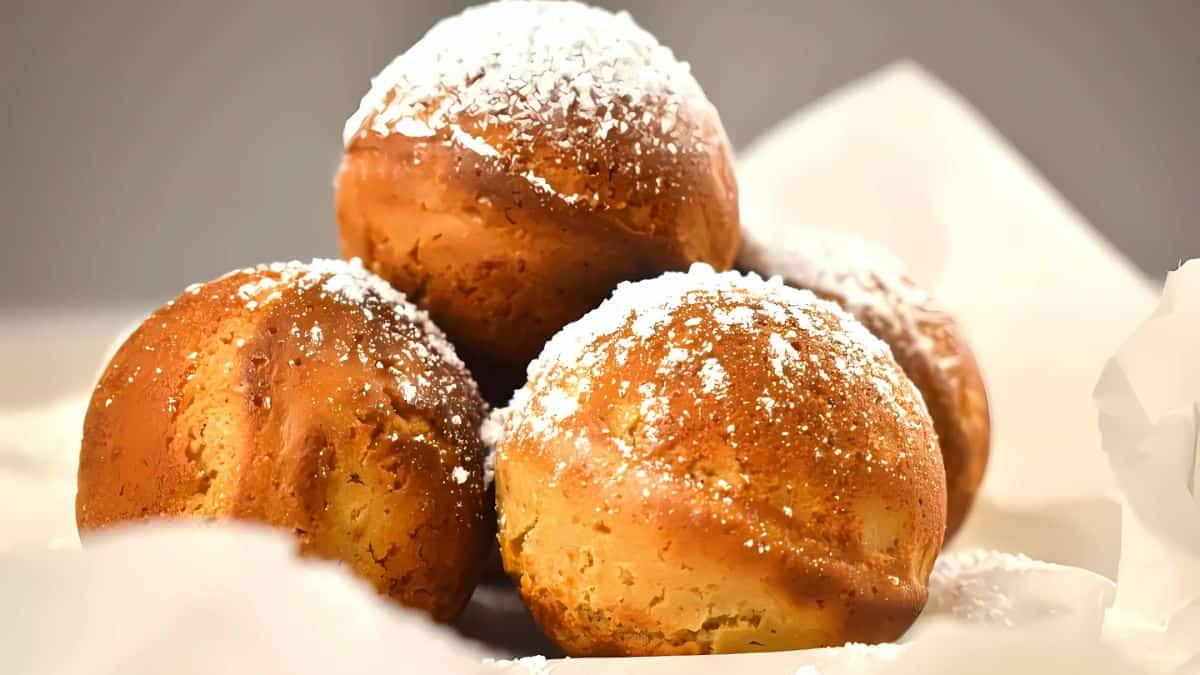 A stack of four golden-brown pastries dusted with powdered sugar set against a parchment paper background. The pastries appear freshly baked and appetizing.