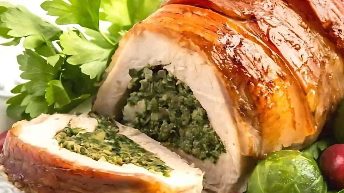 A roasted turkey breast roll stuffed with green spinach filling, sliced to show the stuffing. The dish is garnished with fresh parsley and surrounded by brussels sprouts.