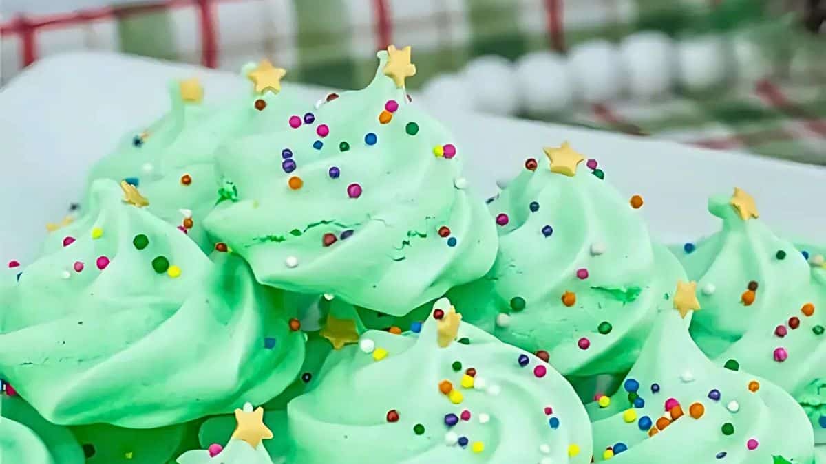 A close-up of festive green meringue cookies sprinkled with colorful confetti and star-shaped decorations, arranged in a pile on a white plate.