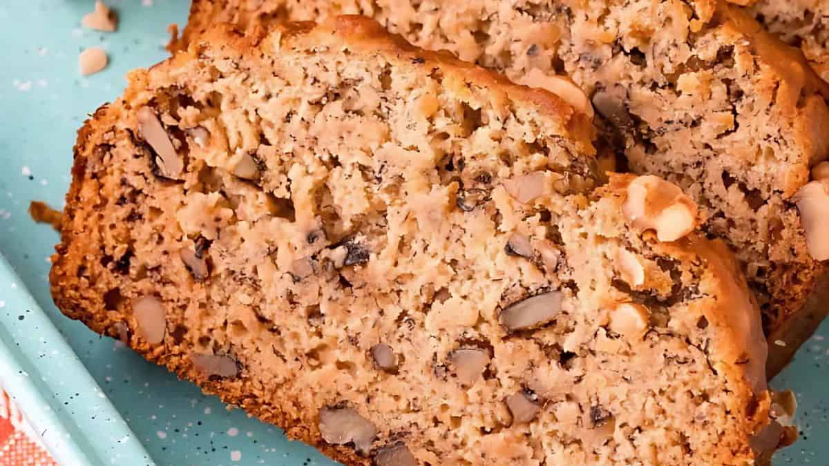 Close-up of sliced banana nut bread on a teal speckled plate. The bread is moist with visible chunks of walnuts and a golden-brown crust.
