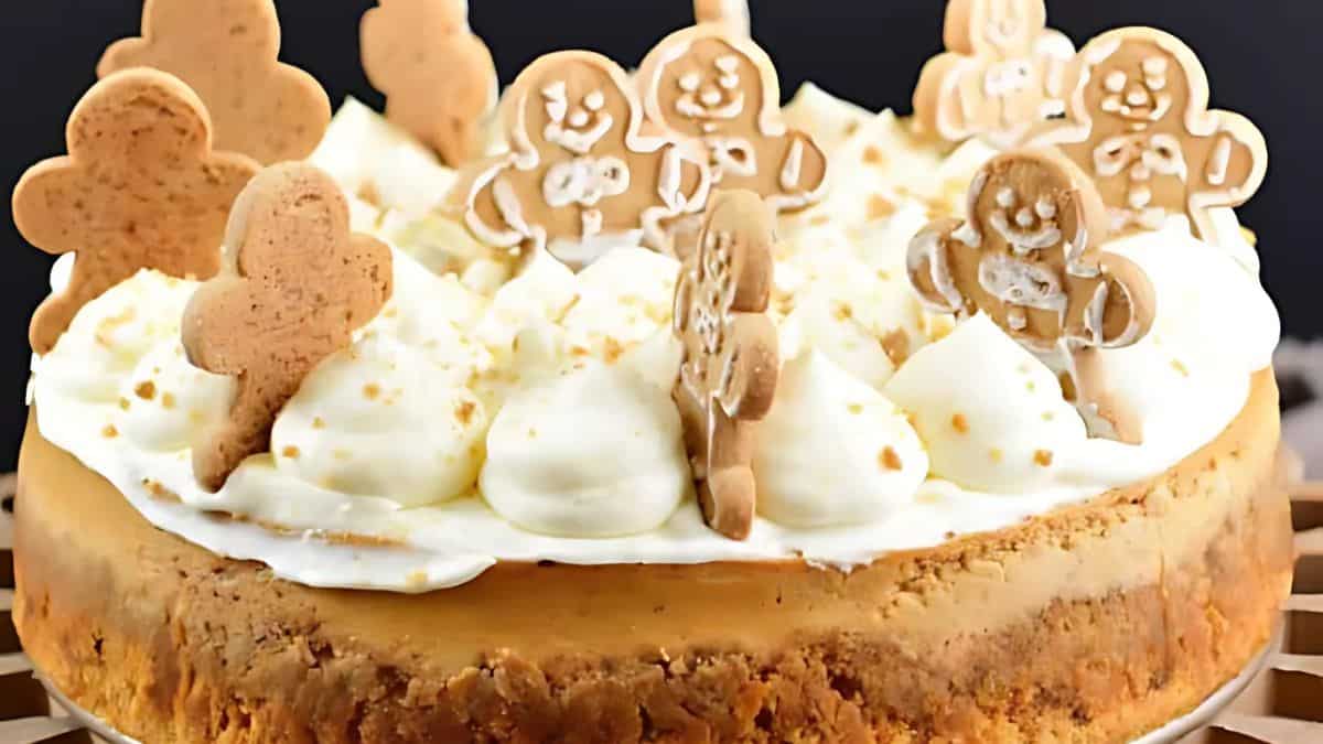 A cheesecake topped with whipped cream and decorated with gingerbread men cookies. The cake has a crumbly crust and the gingerbread men are arranged in a festive, cheerful manner.