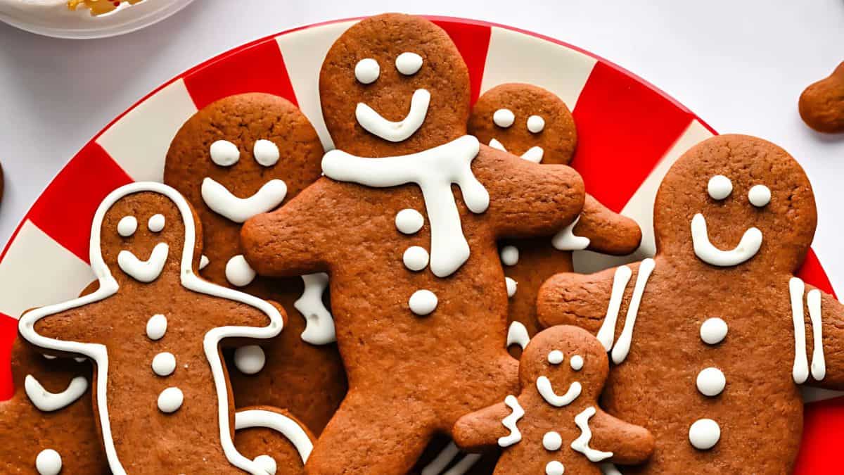 A plate of smiling gingerbread cookies decorated with white icing. The cookies are shaped like people, with scarves and buttons, placed on a red and white striped plate.