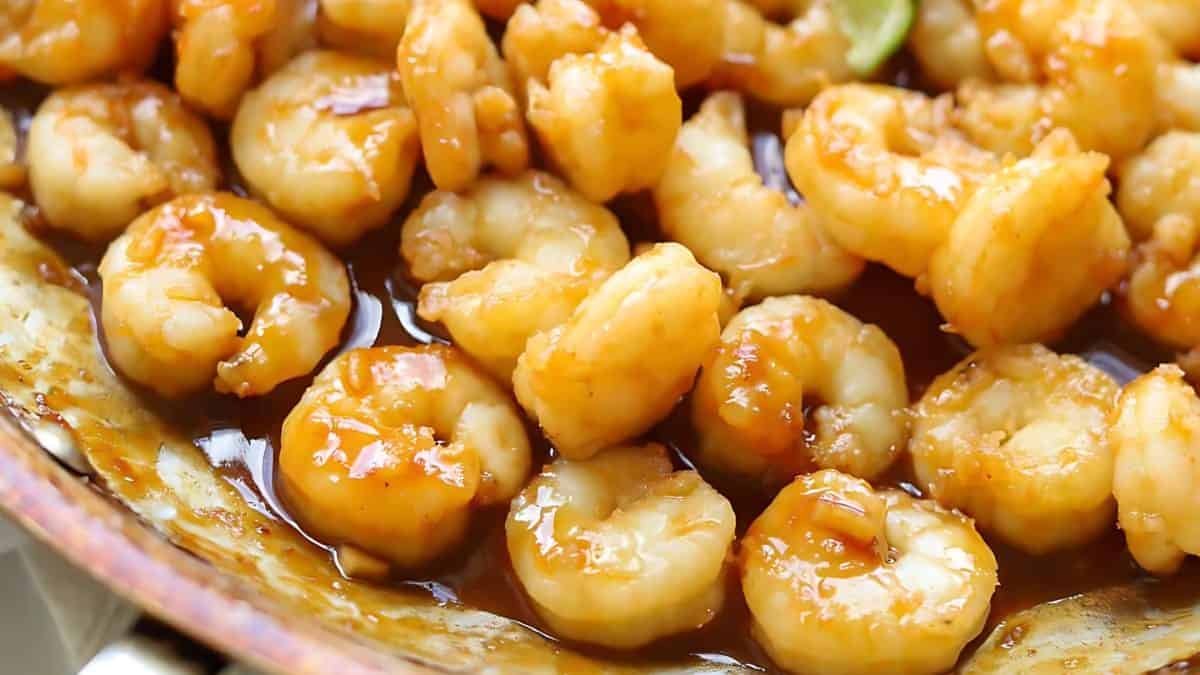 Close-up of cooked shrimp coated in a rich, glossy sauce, filling a pan. The shrimp are golden brown, suggesting they are well-seasoned and flavorful. The dish appears appetizing and ready to be served.