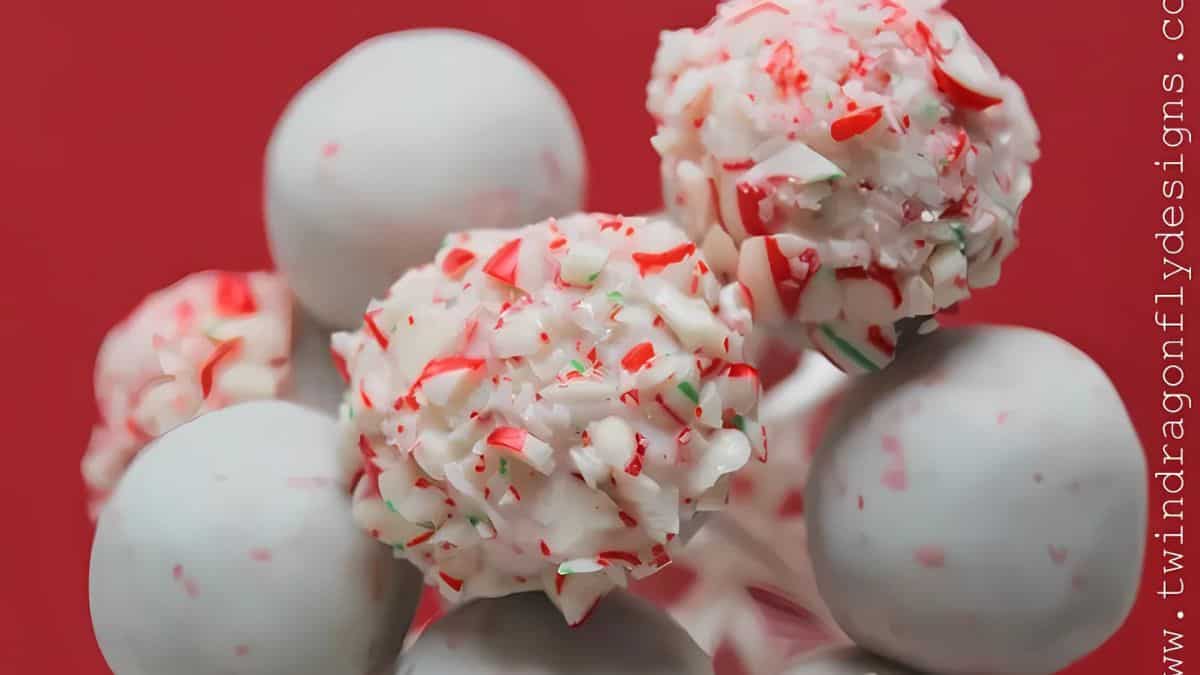 A cluster of white chocolate cake pops, with some topped with crushed candy cane pieces, is arranged against a solid red background. The text "www.twindragonflydesigns.com" is visible vertically on the right.