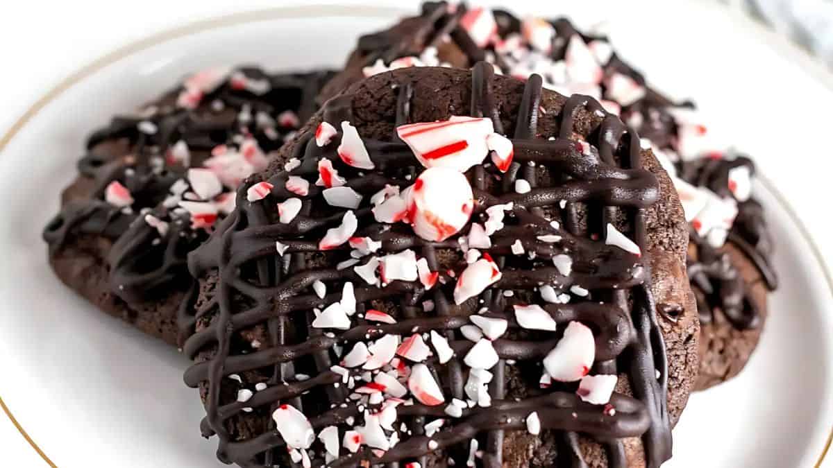A plate of chocolate cookies drizzled with dark chocolate and topped with crushed peppermint pieces.