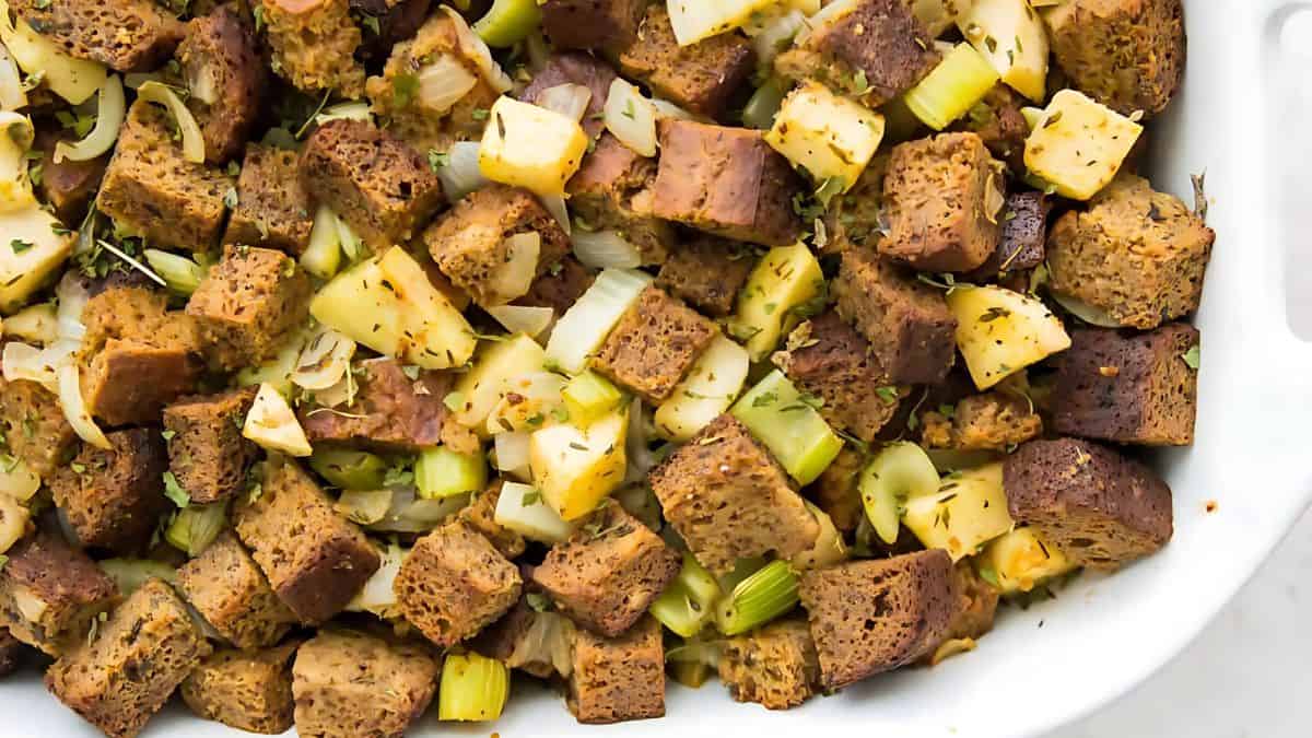 A close-up of a dish featuring cubed bread pieces mixed with chopped vegetables like celery and onion, garnished with herbs. The dish is presented in a white baking dish.