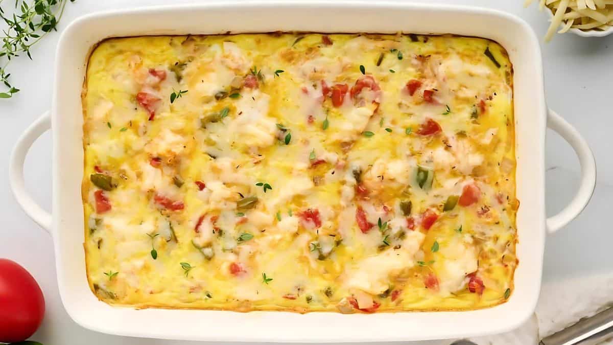 A baked casserole dish filled with a creamy, cheesy mixture featuring diced red and green bell peppers. The top is golden brown with melted cheese and garnished with a few sprigs of fresh thyme.